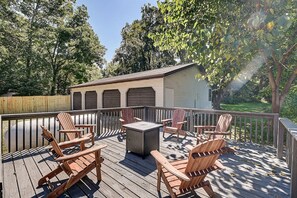 Una terraza con sillas Adirondack y una mesa, rodeada por una valla de madera y árboles.