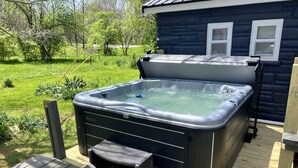Un jacuzzi en una terraza de madera con vista a una casa y follaje.