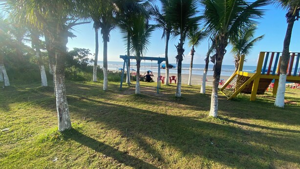 A grassy area with palm trees, a swing set, and a playground structure. - Beach house / Suarão - Itanhaém, 7 minutes walk from the beach. (Itanhaém)