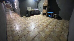 A tiled floor, a sink, a small table, and a brick oven in a dimly lit room. - Beach house / Suarão - Itanhaém, 7 minutes walk from the beach. (Itanhaém)