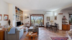 Una sala de estar con un sofá, una mesa de centro, una mesa de comedor con sillas, una estantería y un televisor.