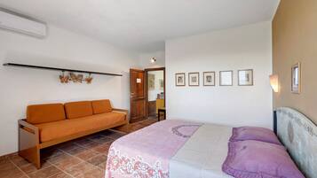 A bedroom with a bed, a sofa, and a wall with framed pictures.