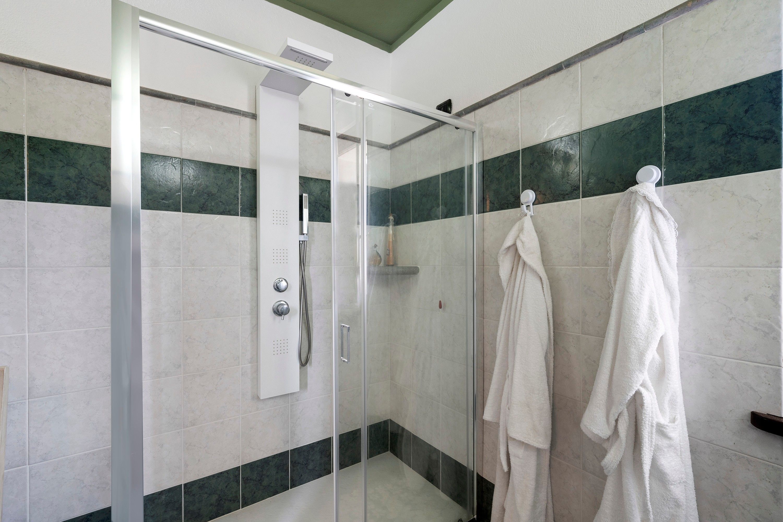 Un espace douche doté d’une porte en verre, d’un pommeau de douche à main et d’un porte-serviettes avec deux serviettes.