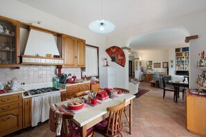Una cuina àmplia amb armaris de fusta, zona de dinar amb taula preparada per a quatre persones, i saló amb sofà i prestatgeries.