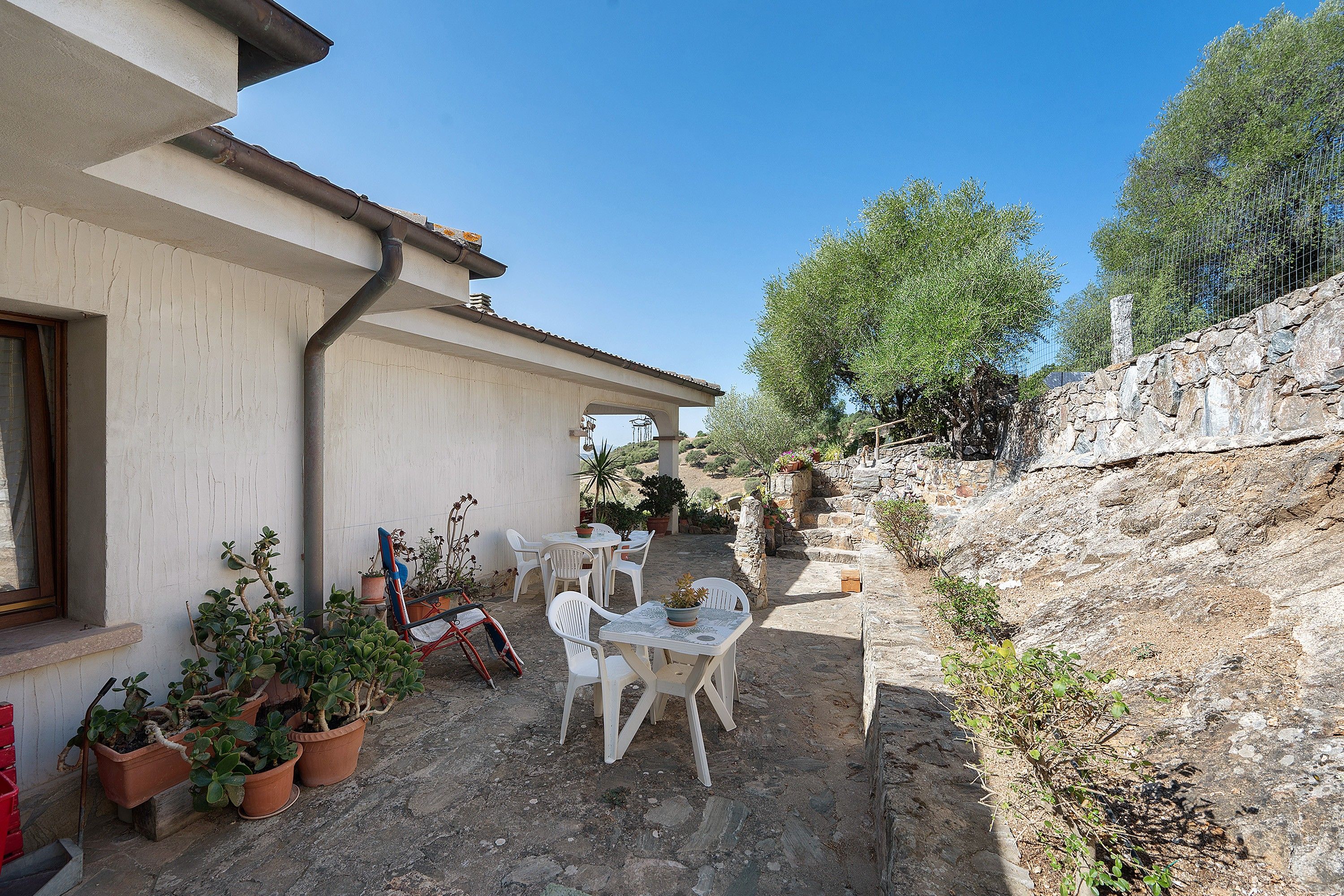 Eine Terrasse mit Gartenmöbeln, Topfpflanzen und einer Steinsäule.