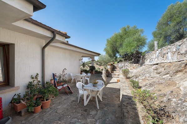 Un patio con mobiliario exterior, plantas en macetas y un muro de piedra.