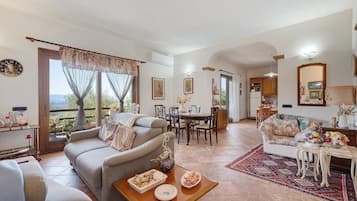 A spacious living room with a sofa, a dining table, and a kitchen area in the background.