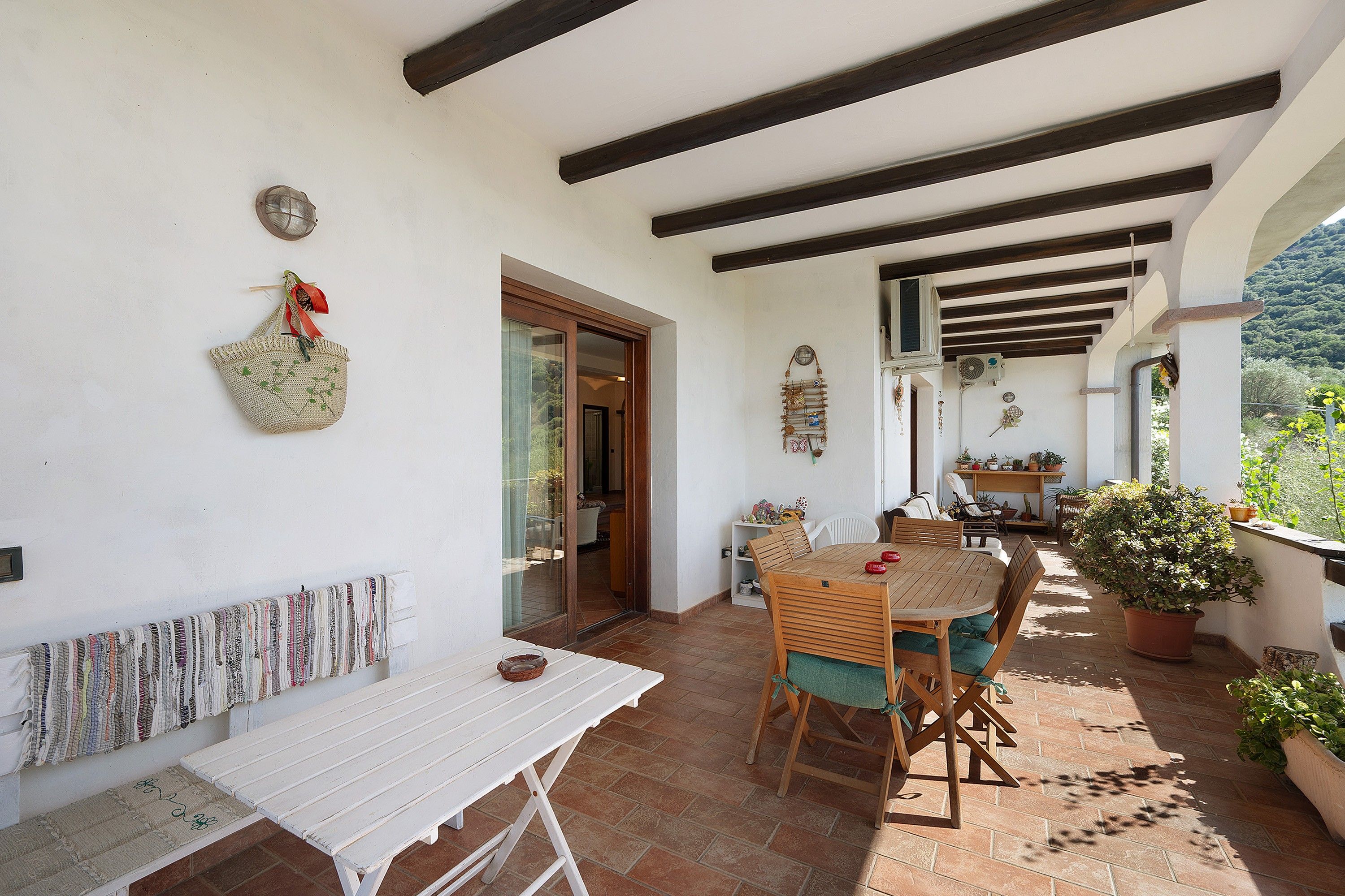 Un portico coperto con tavolo e sedie, una panchina e piante in vaso.