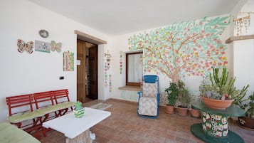 Ein Zimmer mit einer roten Bank, einem weißen Tisch und einem blauen Stuhl. Es gibt Topfpflanzen und eine Wand mit einem gemaltem Baum.