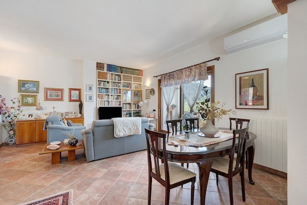 A living room with a sofa, a dining table with chairs, a bookshelf, and a TV.