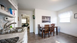 Une cuisine moderne dotée d’un lave-vaisselle intégré, un coin repas avec une table et des chaises, et une œuvre d’art représentant un paysage urbain accrochée au mur.