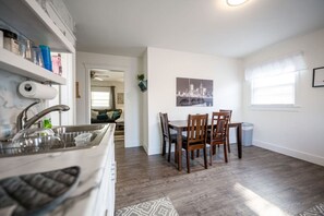 A modern kitchen with a built-in dishwasher, a dining area with a table and chairs, and a cityscape artwork on the wall. - Entire unit-Close to Lucas Oil! (Indianapolis)