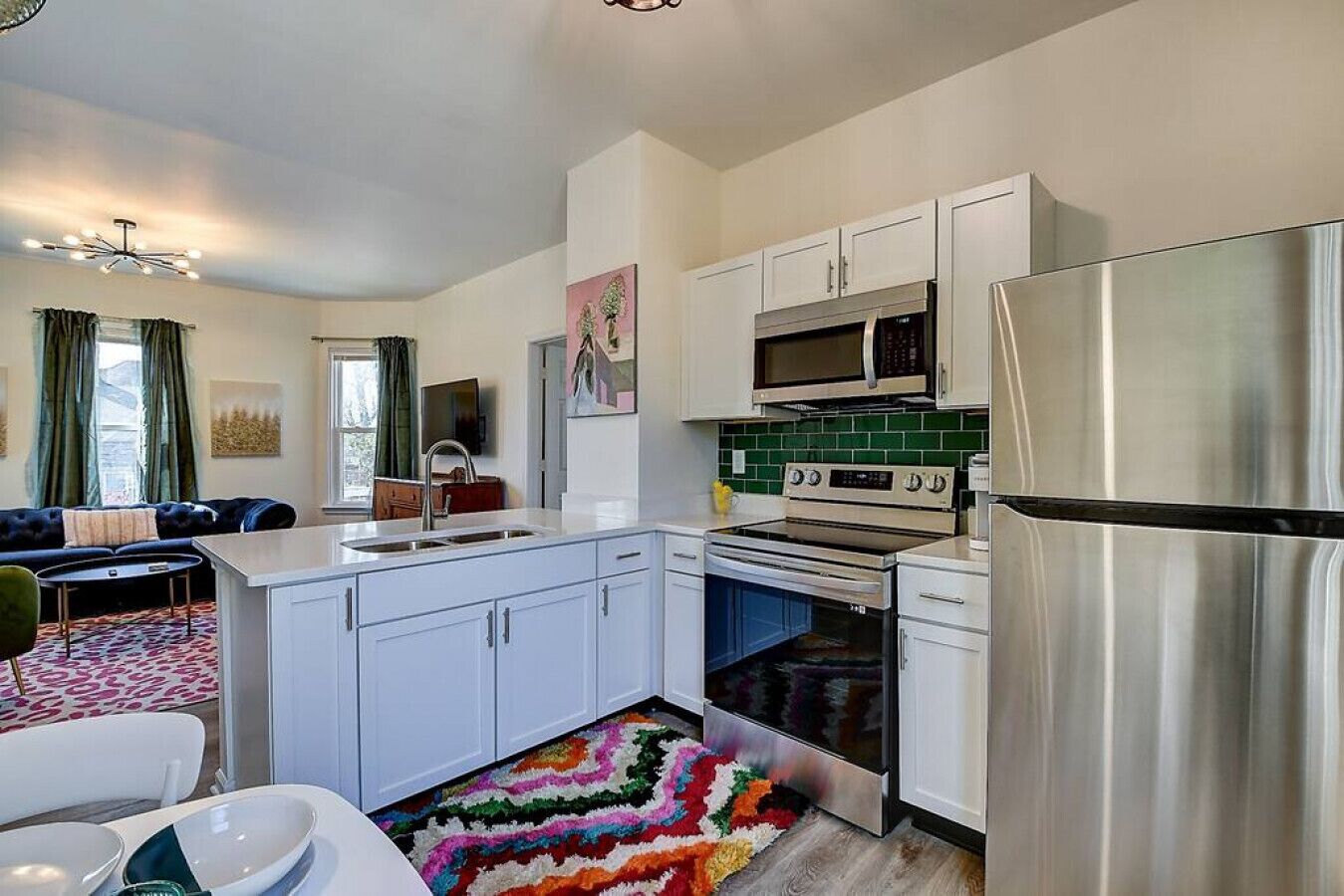A modern kitchen with white cabinets, stainless steel appliances, and a colorful rug.