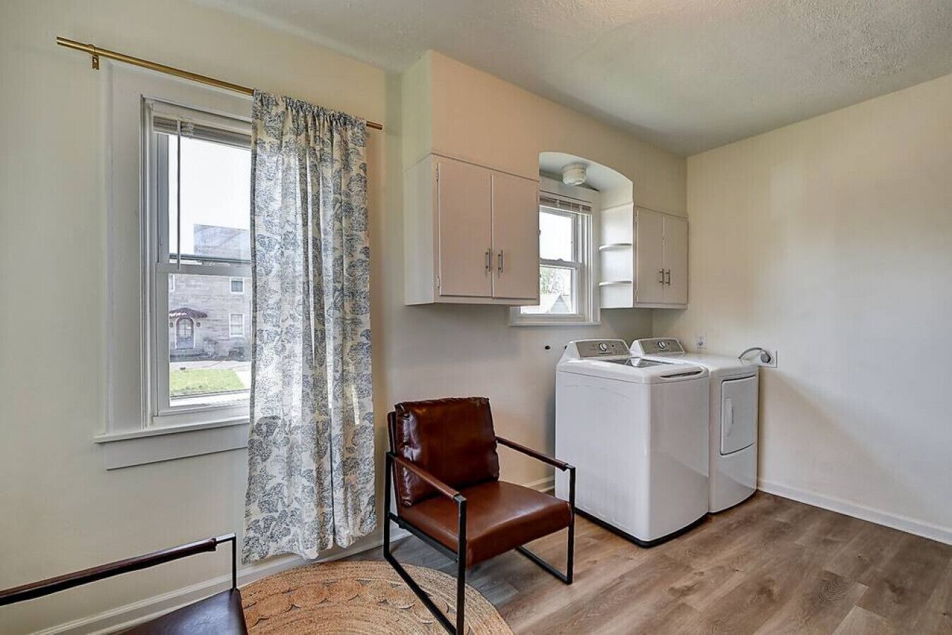 A laundry room with a washing machine, dryer, and a chair.