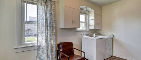 A laundry room with a washing machine, dryer, and a chair.