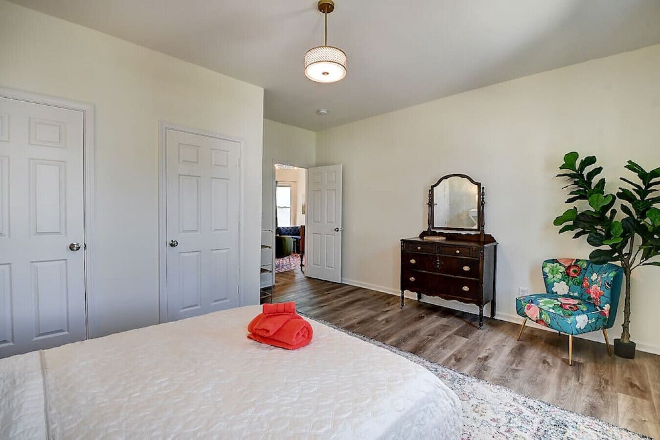 A bedroom with a bed, dresser, chair, and a plant.