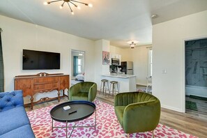 Ein Wohnzimmer mit einer Couch, zwei Sesseln, einem Couchtisch, einem Fernseher und einer Küche im Hintergrund.