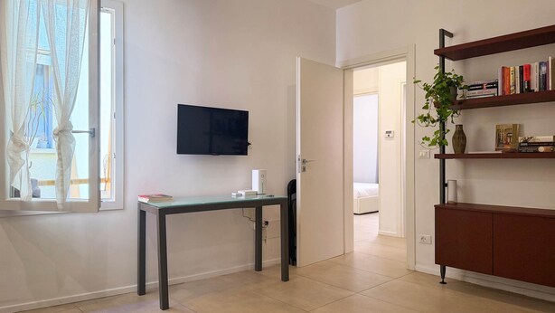 A modern living room with a flat-screen TV, a dining table, a bookshelf, and a door leading to another room. - Casa Accademia in the Heart of Bologna (Bologna)