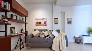 A modern living room with a grey sofa, a bookshelf, a framed artwork, and a potted plant. - Casa Accademia in the Heart of Bologna (Bologna)