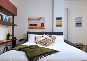 A hotel room with a bed, a shelf with bottles, a poster, and framed pictures on the wall. - Casa Accademia in the Heart of Bologna (Bologna)
