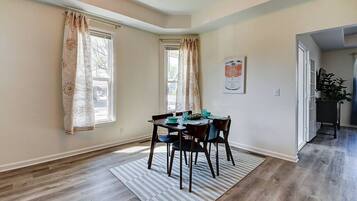 A dining area with a table set for four, a rug, and a window with curtains.