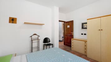 Ein Schlafzimmer mit einem Bett, einem Sessel, einem Kleiderschrank, einem Regal und einer Tür zu einem anderen Raum.