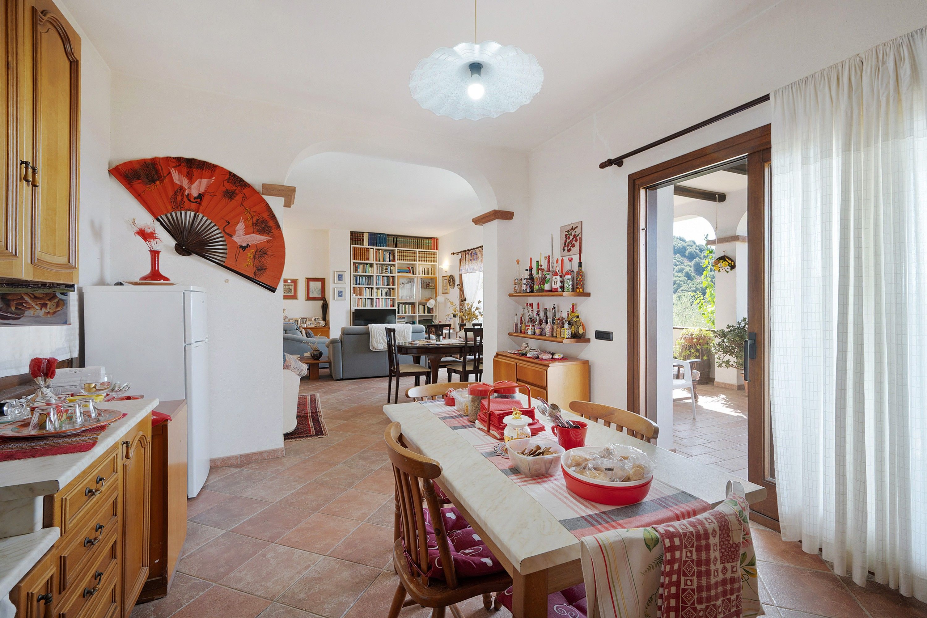 A spacious kitchen with a dining area, a bookshelf, and a view through a glass door.