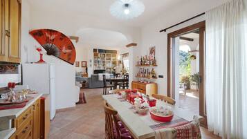 A spacious kitchen with a dining area, a bookshelf, and a view through a glass door.