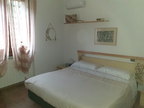 Une chambre à coucher avec un lit, une table de chevet avec une horloge, une étagère murale décorative et une fenêtre avec des rideaux.