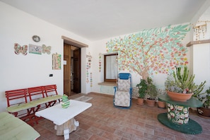 A room with a red bench, a white table, and a blue chair. There are potted plants and a wall with a painted tree. - Double Room with Shared Terrace, Lake View and Wi-Fi (Oschiri)