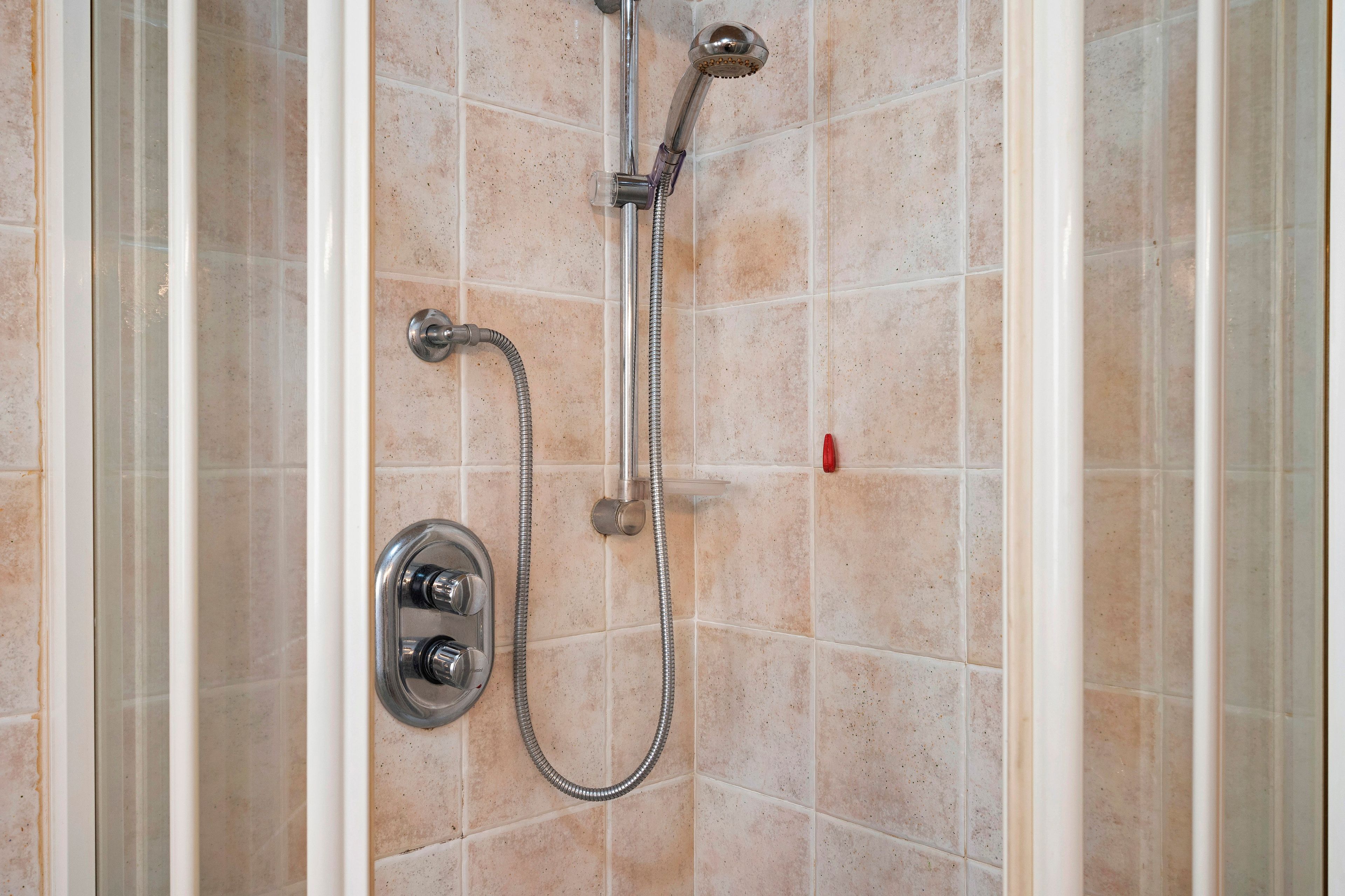 Eine Dusche mit einer verstellbaren Duschbrause und einer fest installierten Duschbrause, beide an einer gefliesten Wand befestigt.