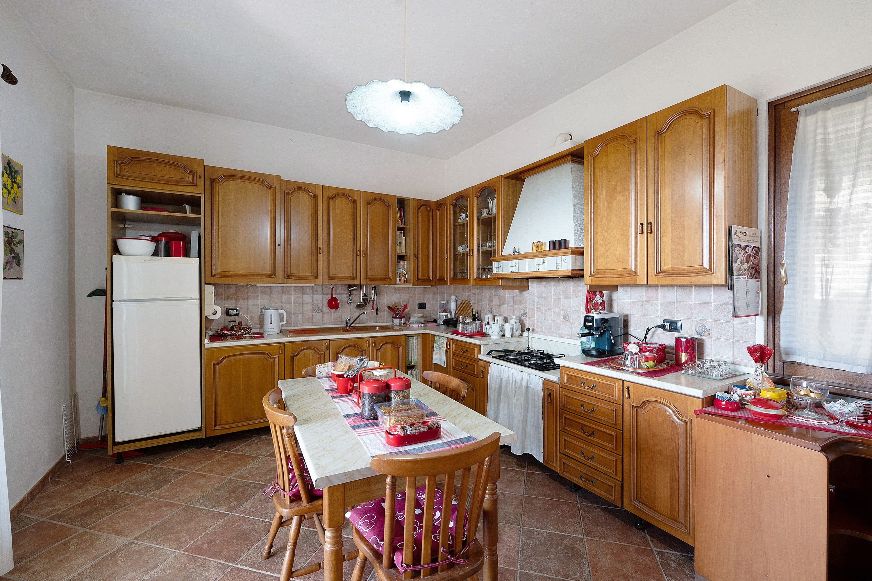 Una cucina con mobili in legno, un tavolo da pranzo con sedie, un frigorifero e diversi elettrodomestici.