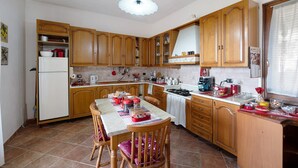 Een keuken met houten kastjes, een eettafel met stoelen, een koelkast en diverse keukenapparaten.