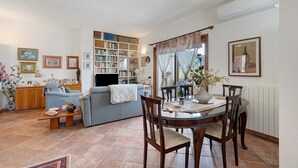 Een woonkamer met een bank, een eettafel met stoelen, een boekenkast en een televisie.