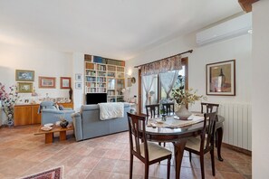 A living room with a sofa, a dining table with chairs, a bookshelf, and a TV. - Double Room with Shared Terrace, Lake View and Wi-Fi (Oschiri)