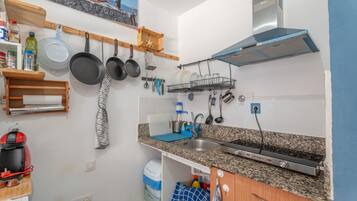 A kitchen with granite countertops, a stainless steel sink, hanging pots, a coffee maker, and a built-in range hood.