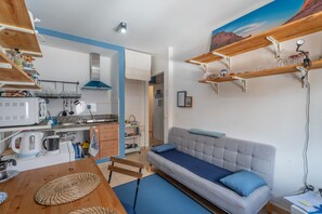 Ein gemütlicher, kompakter Wohnraum mit Küchenzeile, Sofa und einer Wandablage für Gläser.