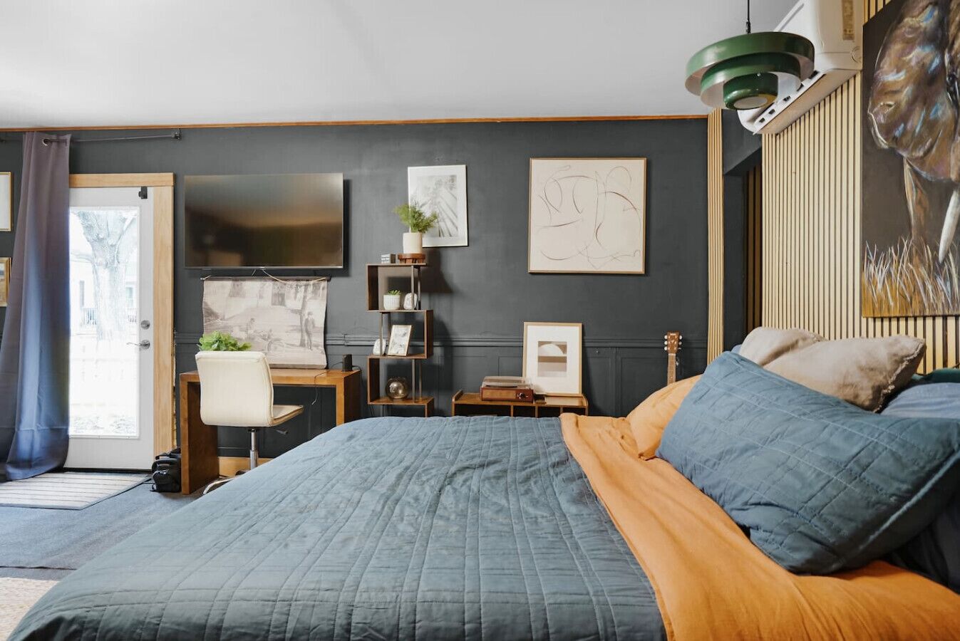 A bedroom with a bed, a desk, a chair, a TV, and artwork on the walls.