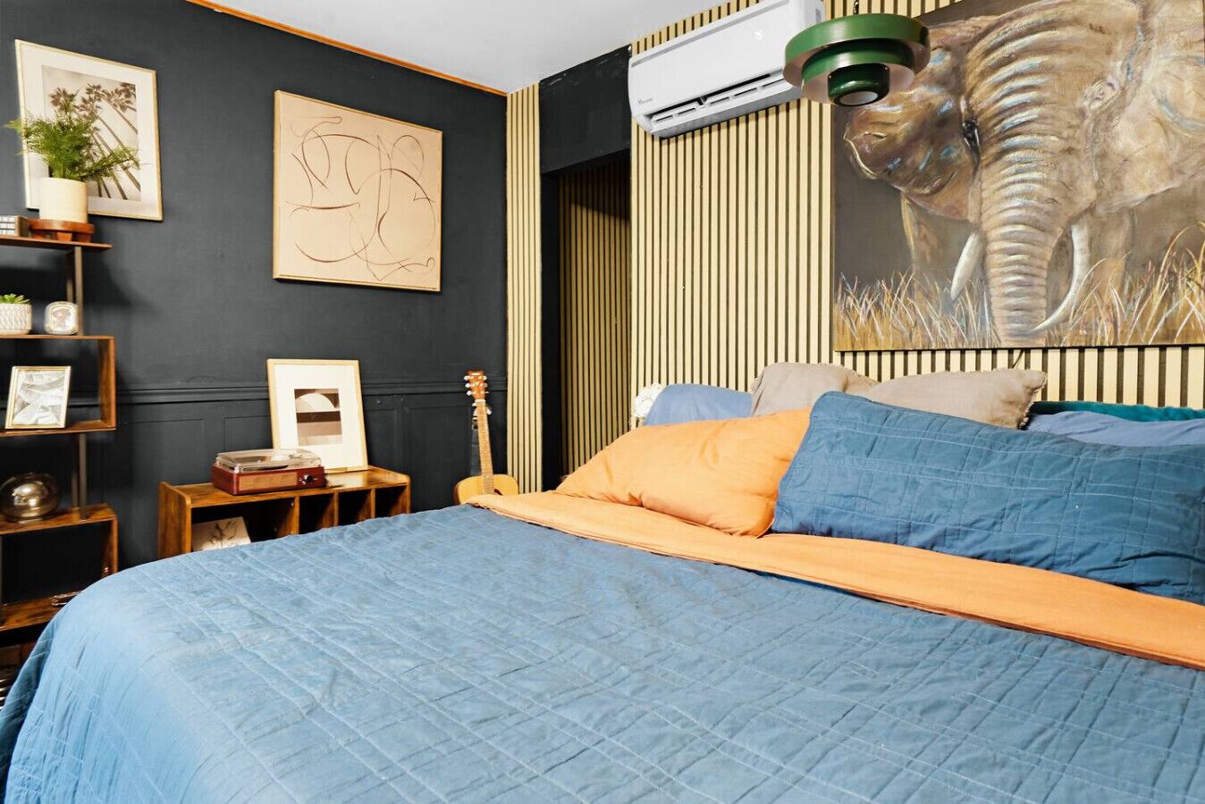 A bedroom with a large bed, a guitar, a framed picture, and a wall-mounted air conditioner.