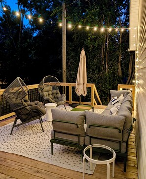 Eine Terrasse im Freien mit einer Sofagruppe, einem Sessel, einem kleinen Tisch und Lichterketten.