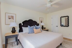 A bedroom with a large bed, two bedside tables with lamps, a ceiling fan, and artwork on the walls.