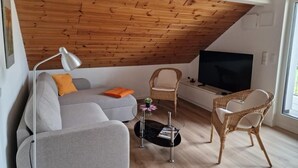 A modern living room with a sloped ceiling, a sofa, a coffee table, wicker chairs, and a flat-screen TV. - NEW! Vacation apartment Zapfe Schnabelwaid (Schnabelwaid)