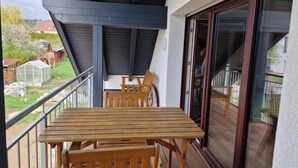 A balcony with a wooden table and chairs, a glass door, and a view of a garden and buildings. - NEW! Vacation apartment Zapfe Schnabelwaid (Schnabelwaid)