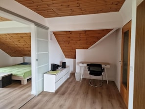 A room with a sloped ceiling, a bed, a desk with a chair, and a white dresser.