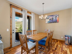 A dining area with a wooden table and chairs, a chandelier, a painting on the wall, and a view through a sliding door. - Mins to Park City & Deer Valley! 4BR Townhome (Hideout)