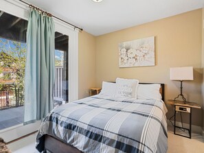 A bedroom with a large bed, a view to the outside, a painting on the wall, and a bedside table with a lamp. - Mins to Park City & Deer Valley! 4BR Townhome (Hideout)