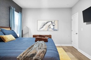 Un dormitorio con cama, televisor montado, pintura de un caballo y suelo de madera.