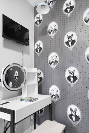 Una habitación con un espejo de tocador, un televisor fijado a la pared y un papel pintado con ilustraciones de perros.