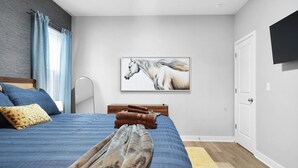 A bedroom with a bed, a mounted TV, a painting of a horse, and a wooden door. - Luxe Downtown Townhome-Sleeps 6 Brand New Build! (Indianapolis)