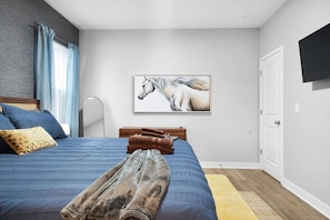 A bedroom with a bed, a mounted TV, a painting of a horse, and a wooden door. - Luxe Downtown Townhome-Sleeps 6 Brand New Build! (Indianapolis)
